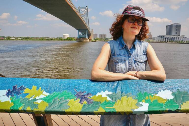 Julie Woodard poses near the tarp artwork that she created for a public installation piece. In the background is the Delaware River.