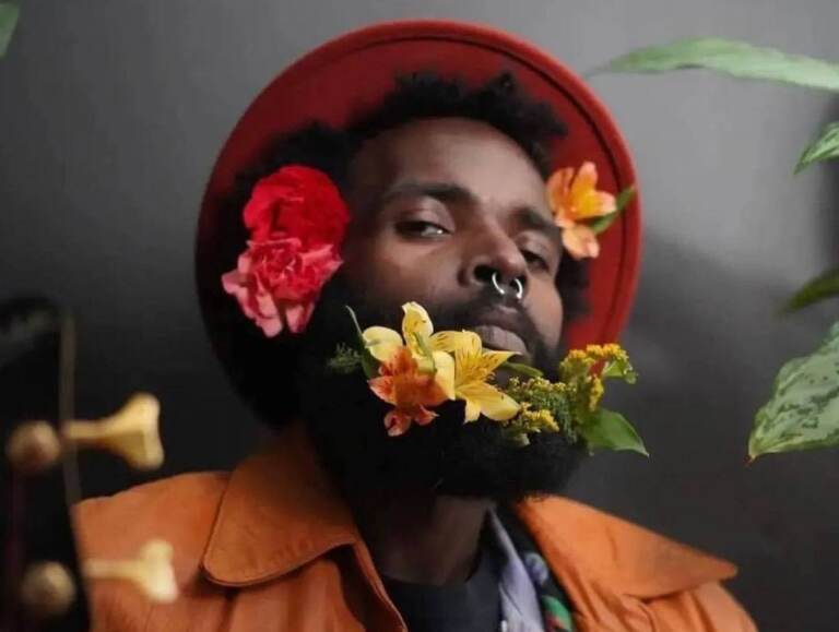 A portrait of Yeho Bostick, posing for a photo with flowers in his beard.