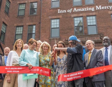 A group of people gathered together cut a ribbon