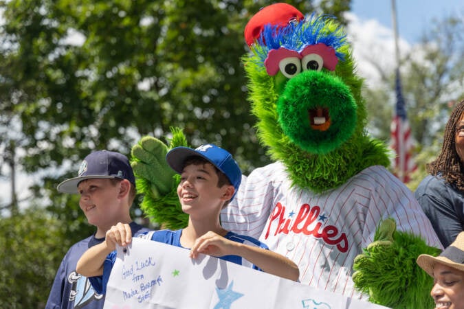 The Philadelphia Phanatic, official mascot of the city’s MLB team, stood behind Joseph Flounders, 12, as Media Borough cheered for their 12U baseball team that will complete in the Little League World Series in Williamsport, Pa., on Aug. 16, 2023. (Kimberly Paynter/WHYY)