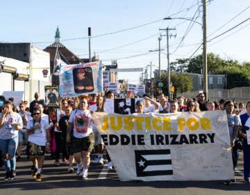 Marchers walk down the street, displaying signs and a large banner that reads 