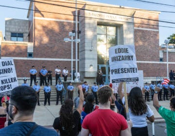 Marchers hold signs and stand in front of a row of police officers outside of the district headquarters.