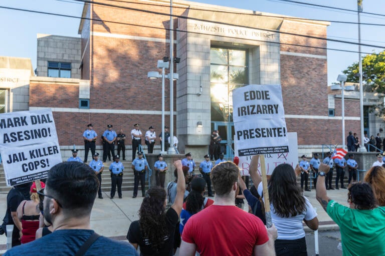 Marchers hold signs and stand in front of a row of police officers outside of the district headquarters.