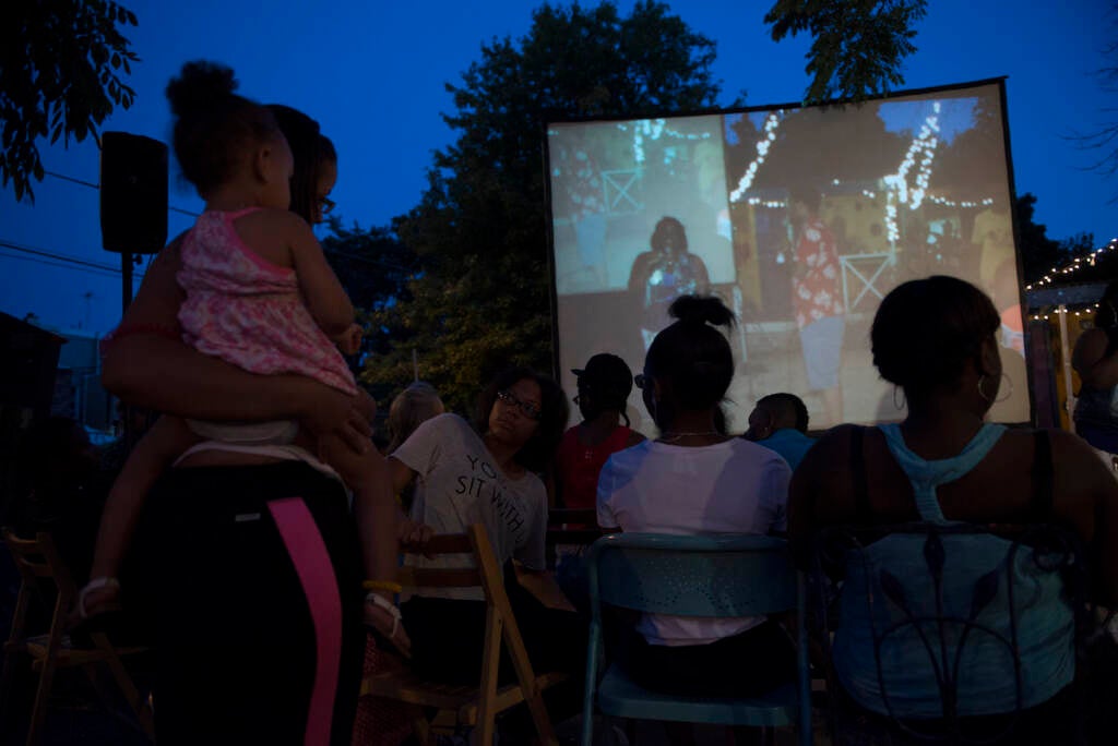 People watch a movie on a projector screen outdoors.