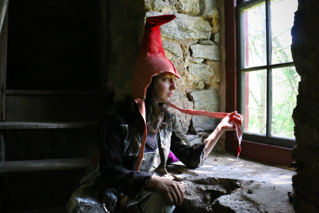 Artist in residence Alex Tatarsky strikes a contemplative pose in the stone water tower at Glen Foerd while wearing a garden hermit hat.