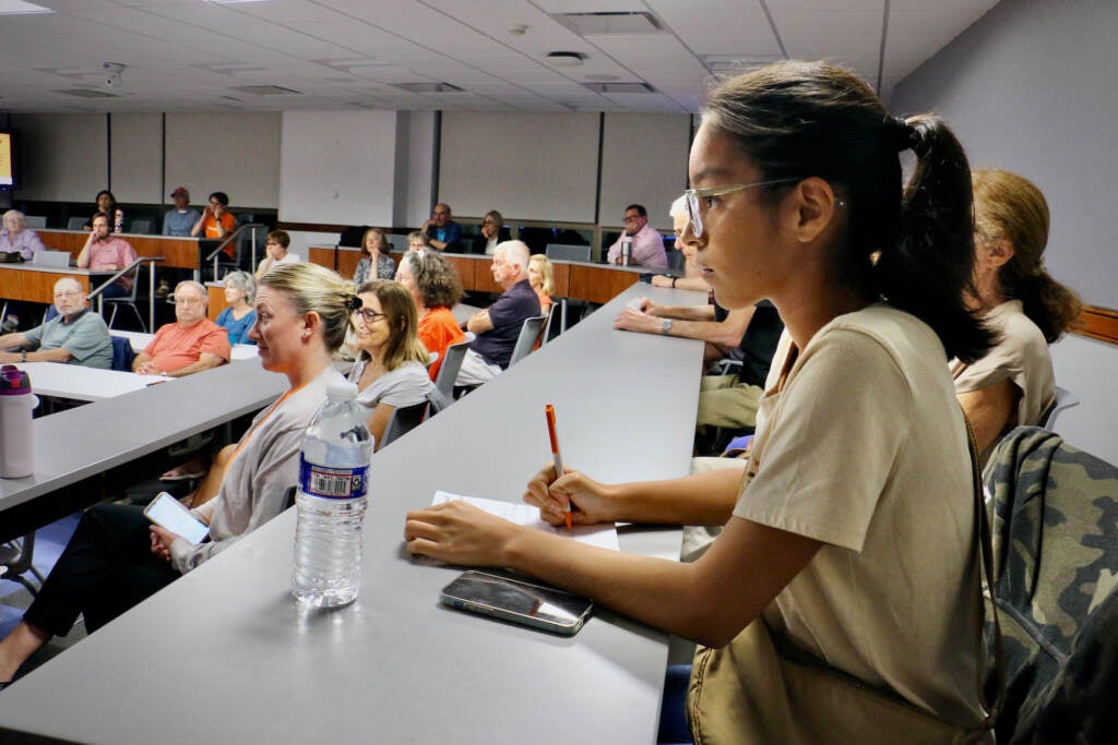 A student takes notes during a town hall meeting