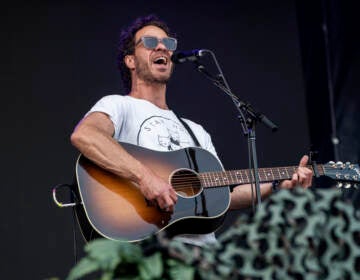 Amos Lee performs at Railbird Music Festival on Sunday, June 4, 2023, at The Infield at Red Mile in Lexington. He is holding a guitar in his hands and sings into a microphone.