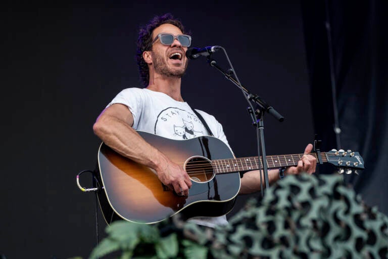 Amos Lee performs at Railbird Music Festival on Sunday, June 4, 2023, at The Infield at Red Mile in Lexington. He is holding a guitar in his hands and sings into a microphone.