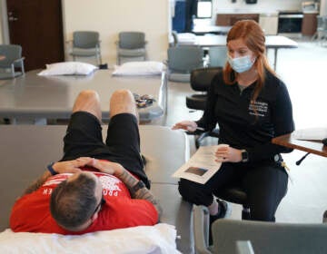 Patient Mike Camilleri works with physical therapist Beth Hughes in St. Louis, Mo., on March 1, 2023. Somehow, a mild case of COVID-19 set off a chain reaction that eventually left Camilleri with dangerous blood pressure spikes, a heartbeat that raced with slight exertion, and episodes of intense chest pain.