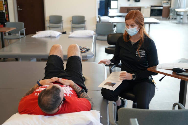 Patient Mike Camilleri works with physical therapist Beth Hughes in St. Louis, Mo., on March 1, 2023. Somehow, a mild case of COVID-19 set off a chain reaction that eventually left Camilleri with dangerous blood pressure spikes, a heartbeat that raced with slight exertion, and episodes of intense chest pain.