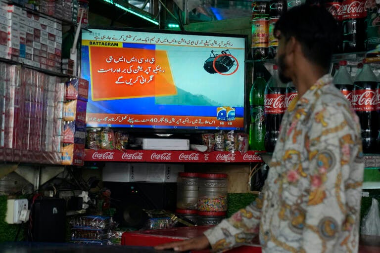 A shopkeeper watches a news channel airing news regarding people trapped in a cable car, at his shop in Lahore, Pakistan, Tuesday, Aug. 22, 2023. A cable car carrying six children and two adults dangled hundreds of meters (feet) above the ground in a remote part of Pakistan after it broke on Tuesday, trapping the occupants for hours before rescuers arrived in helicopters to try to free them.