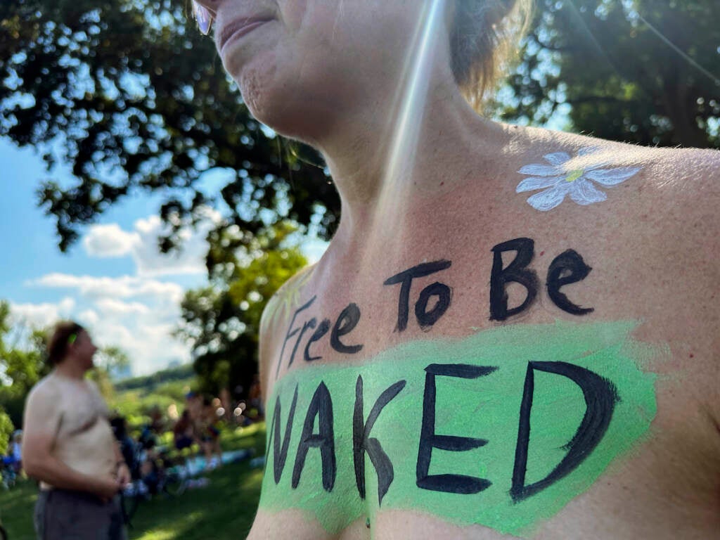 A woman with the phrase “Free To Be Naked” on her bare chest.