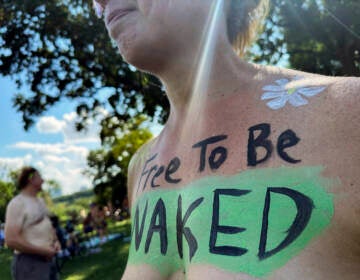 A woman with the phrase 'Free To Be Naked' written across her bare chest.