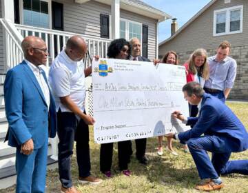 Matt Meyer signs a check held by several other people in front of a new home.