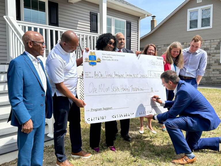 Matt Meyer signs a check held by several other people in front of a new home.