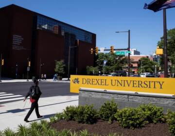 A person walks by a sign reading Drexel University.