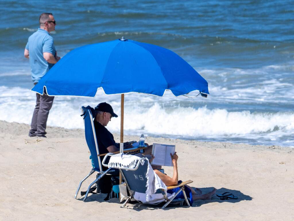 A U.S. Secret Service officer stands watch as President Biden and first lady Jill Biden sit under an umbrella in Rehoboth Beach on Sunday.