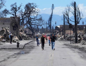 People walk down a road with damaged and burned wreckage visible on either side