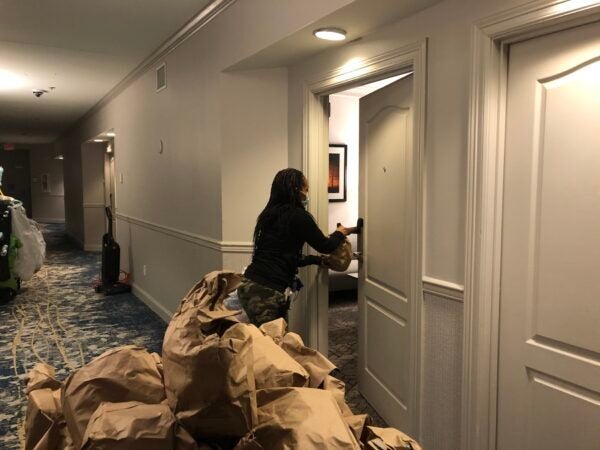 A woman with many supplies knocking on a hotel door.