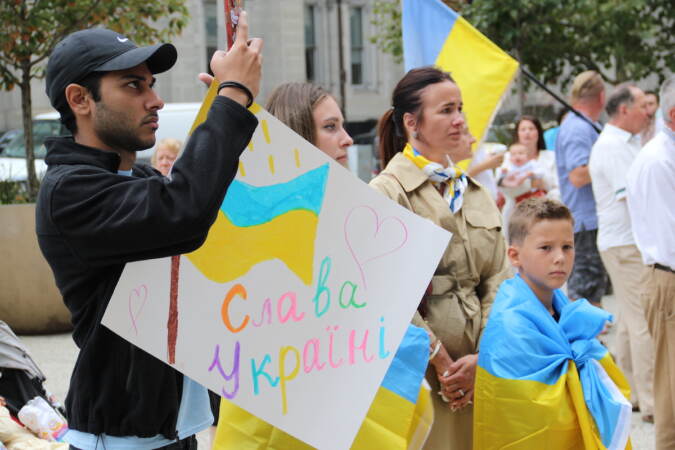 Children and adults stand holding, wearing Ukrainian flags.