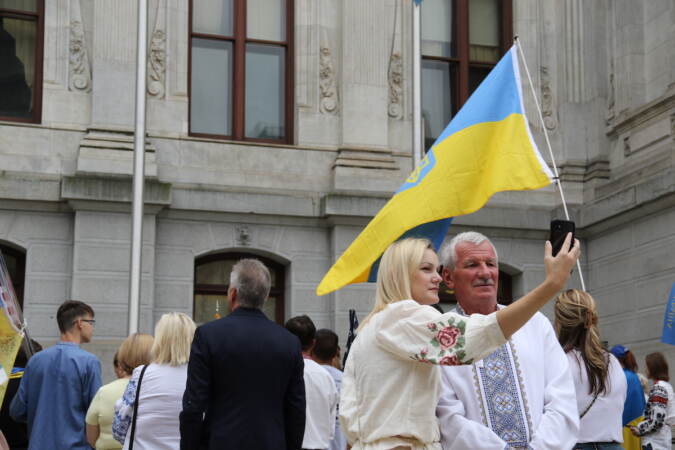 A person takes a picture with someone else as a Ukrainian flag flies in the background.