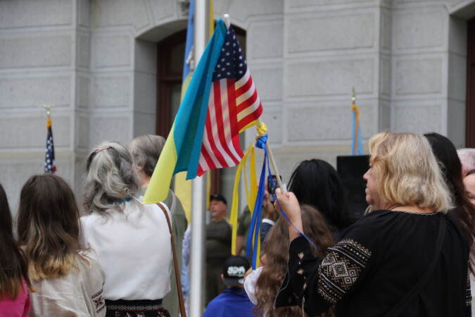 Ukrainian and American flags seen together being held up by someone in a crowd