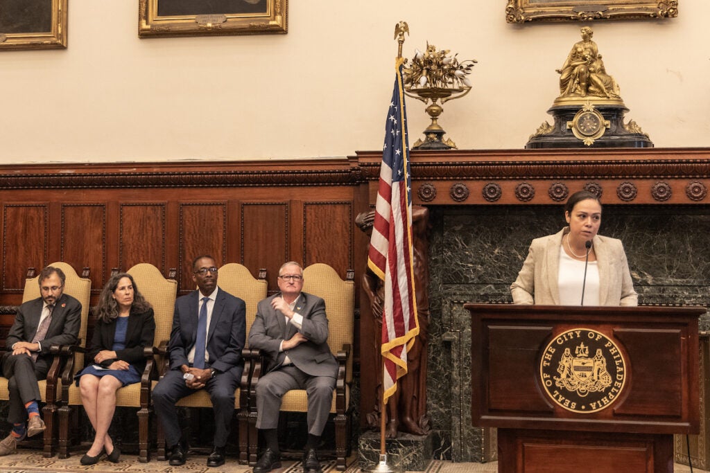 Philadelphia City Solicitor Diana Cortes (right) speaks at a podium as city officials seated to the left look on.