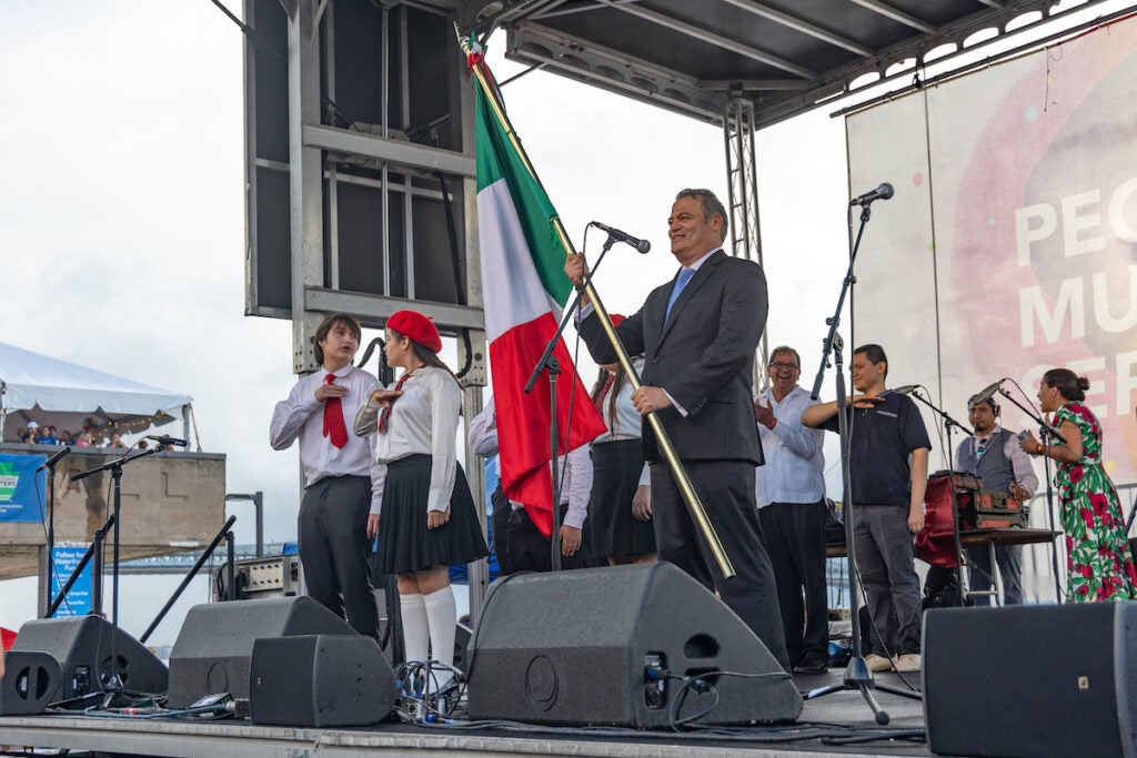 Carlos Obrador Garrido holds the Mexican flag as he stands with other people onstage.