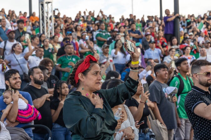 A woman in the foreground places her hand over her heart as she holds up her phone with the other hand. The other attendees in the crowd do the same.