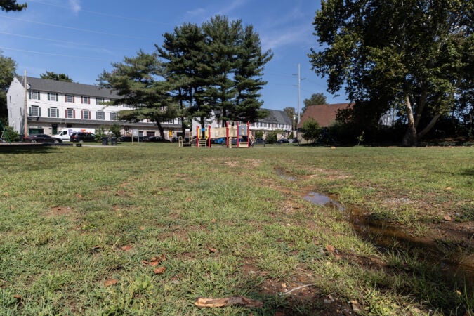 A puddle of water is visible in a field. Homes are visible in the distance.