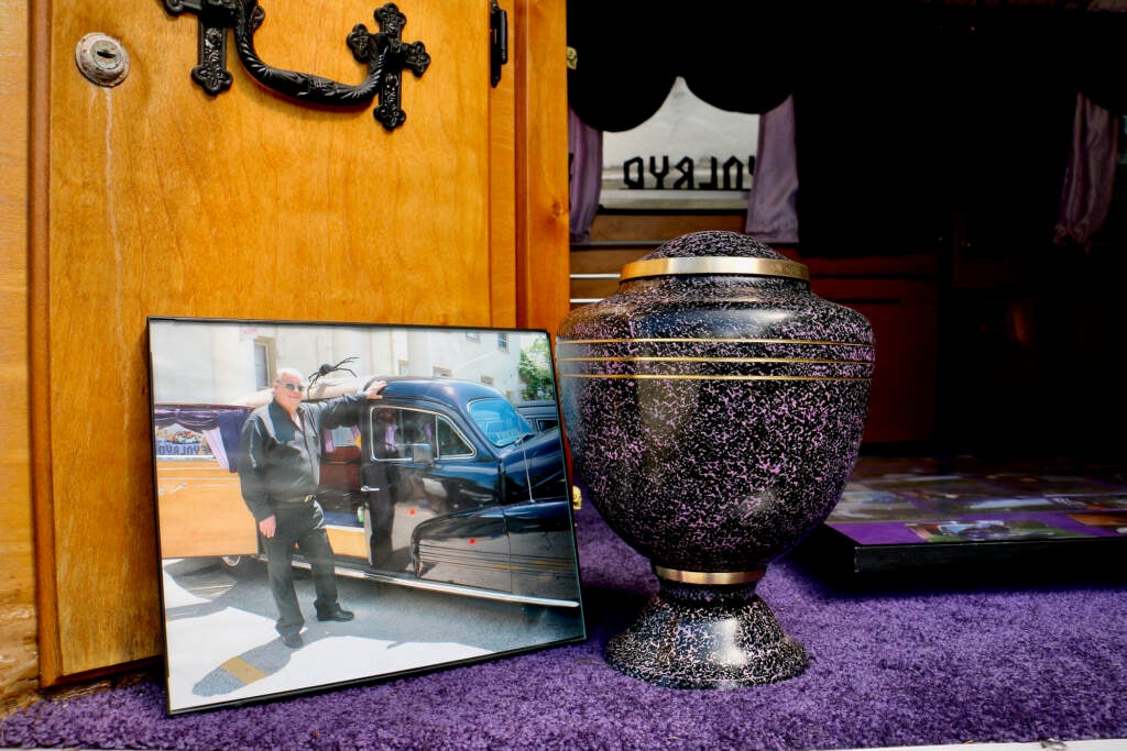 A photo of Russ Slegel next to an urn containing his ashes inside of the purple hearse he owned