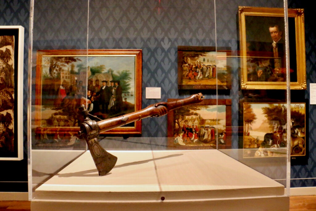 This pipe tomahawk made in the late 18th to early 19th century was likely intended to be presented during a treaty agreement. It is placed beside some of the many painted versions of the Penn Treaty with the Indians, an agreement that pushed the Lenape west