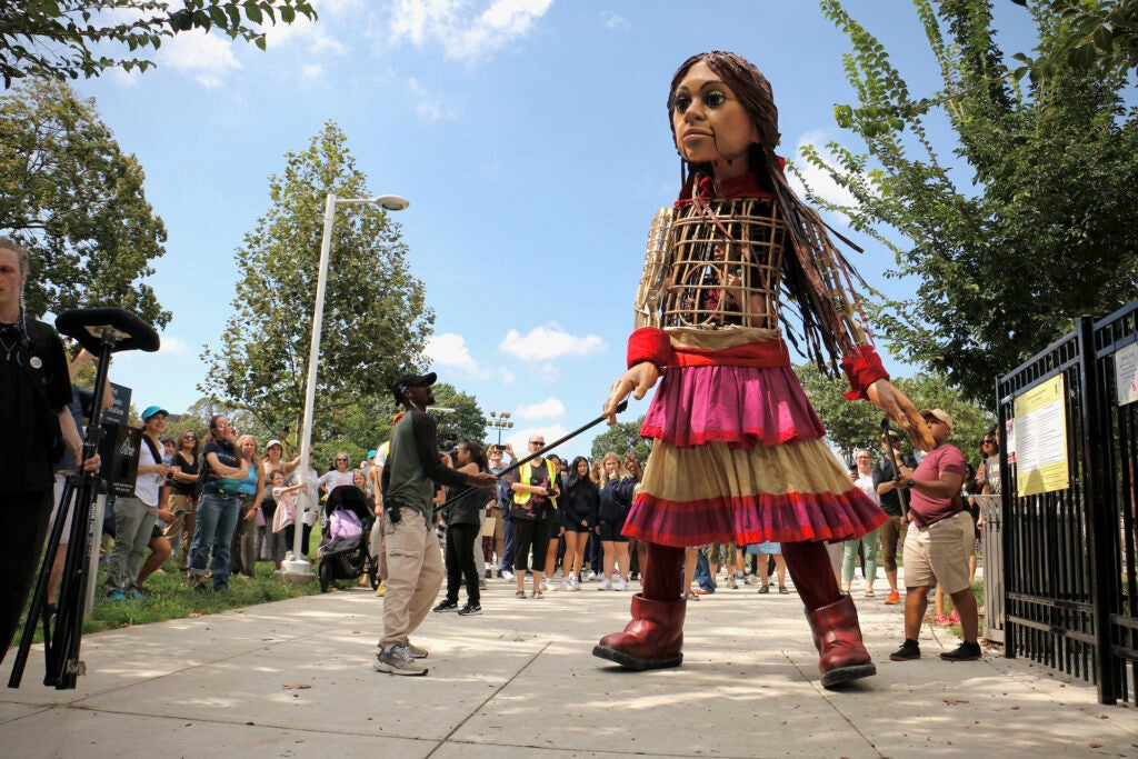 Little Amal, a 12-foot-tall puppet operated by three people, stands on the sidewalk in South Philadelphia.