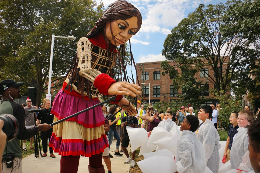 Little Amal, a 12-foot-tall puppet, reaches out towards a group of fifth graders.