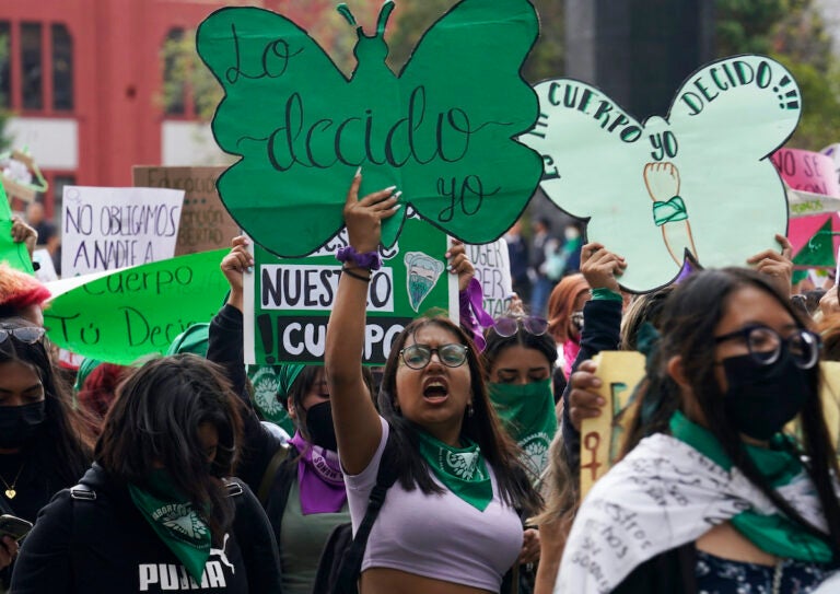 A woman holds up a sign with a message that reads in Spanish; 