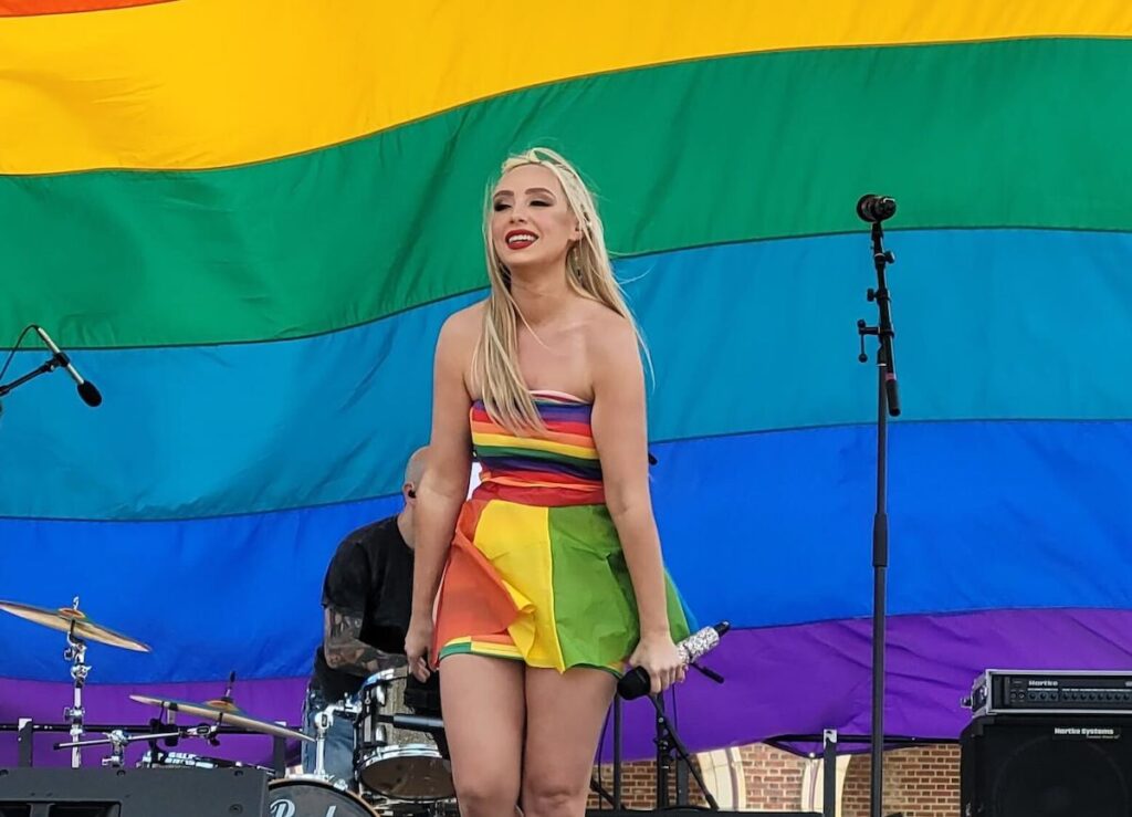 Kariselle Snow onstage, with a giant Pride flag hanging behind her.