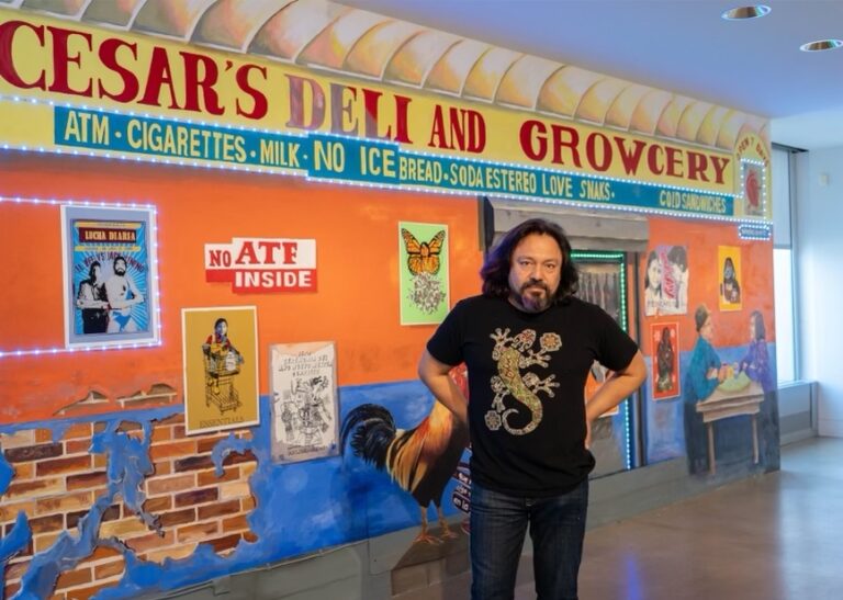 Cesar Viveros poses for a photo in front of a mural and installation at the Delaware Art Museum