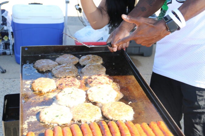 Theo Nugin points to burgers and hot dogs that he's grilling