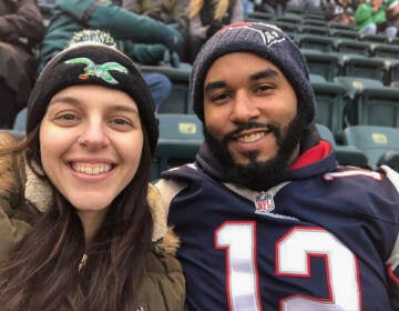 A woman wearing a Philadelphia Eagles hat, and a man wearing a New England Patriots jersey and hat