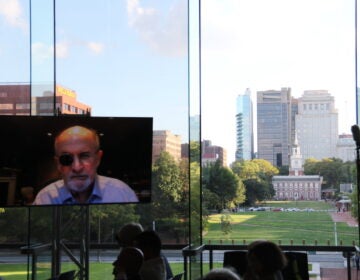 Salman Rushdie speaks from a screen. Behind the screen are windows looking out over Independence Hall.