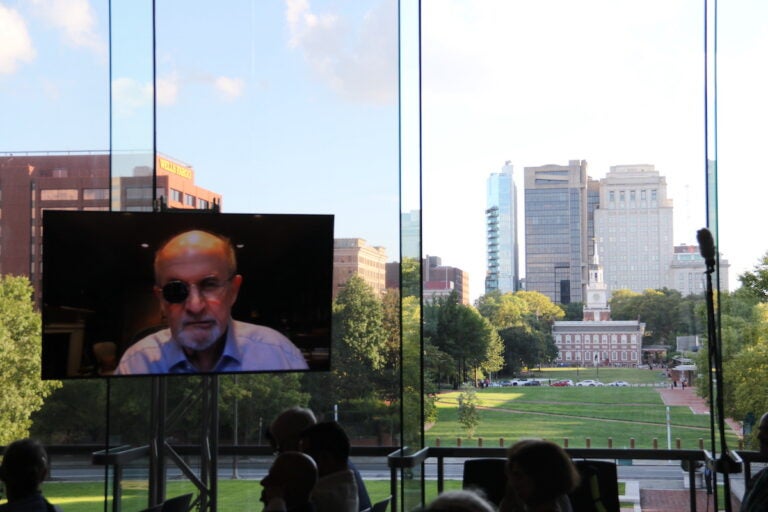 Salman Rushdie speaks from a screen. Behind the screen are windows looking out over Independence Hall.