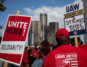 Striking auto workers hold signs.