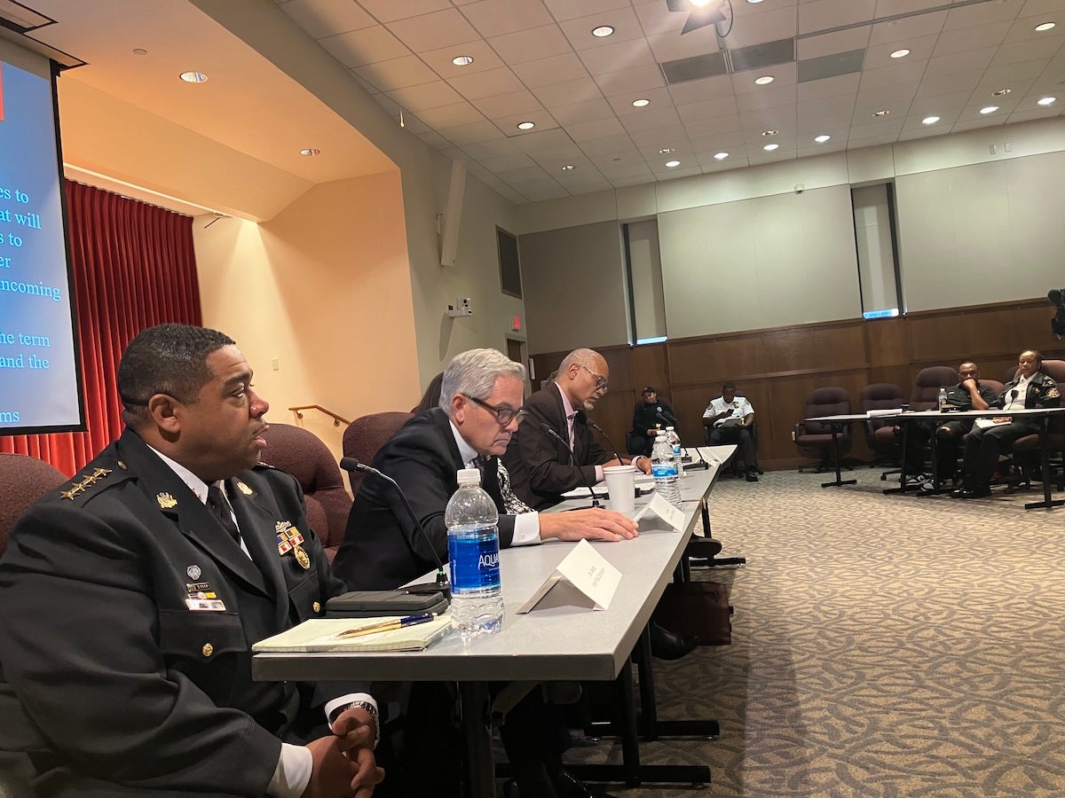 From left, Interim PPD Commissioner John Stanford, District Attorney of Philadelphia Larry Krasner and others participate in a panel, seated at a table, with a slideshow visible behind them.