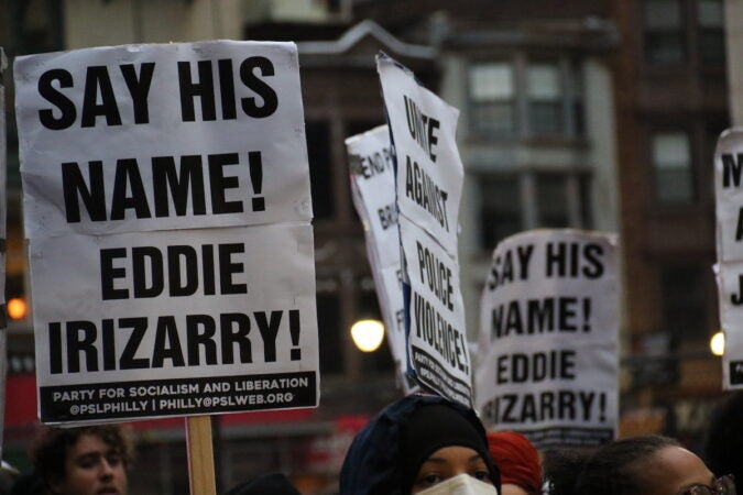 Prosters hold signs that read Say his name! Eddie Irizarry!