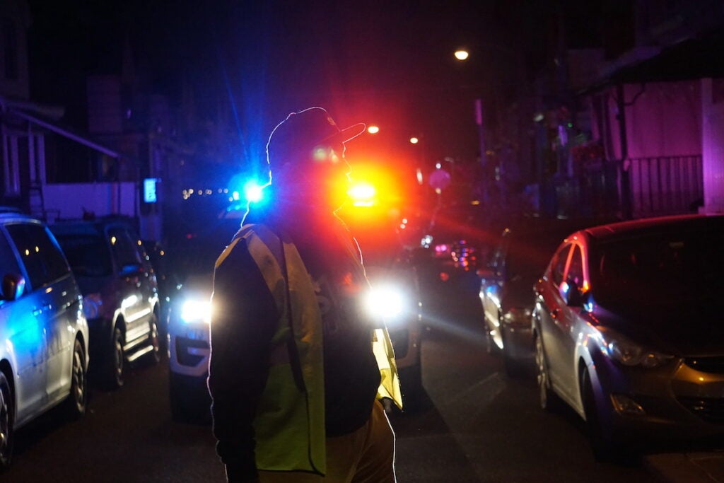 Jamal Johnson walks in a street at night wearing a yellow safety vest.