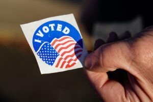 An up-close view of someone holding an I Voted sticker featuring the U.S. flag.