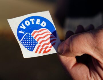 An up-close view of someone holding an I Voted sticker featuring the U.S. flag.