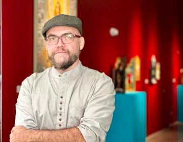 Patrick McGrath Muñiz poses for a photo. His paintings are visible behind him.