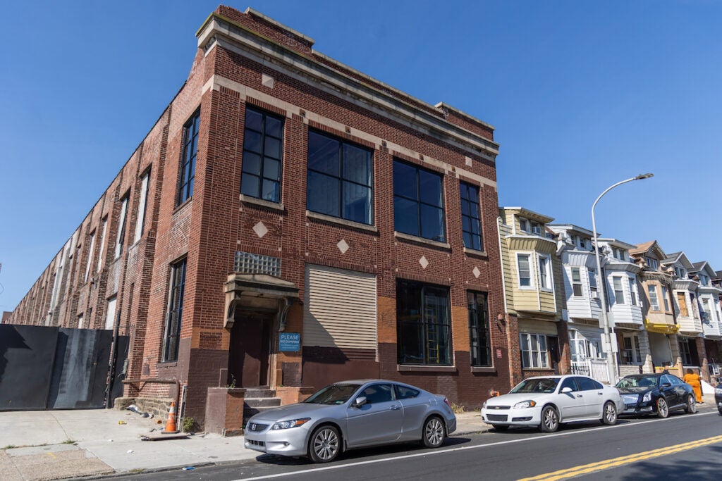 A former factory building being turned into a high school is visible on a street of rowhomes.