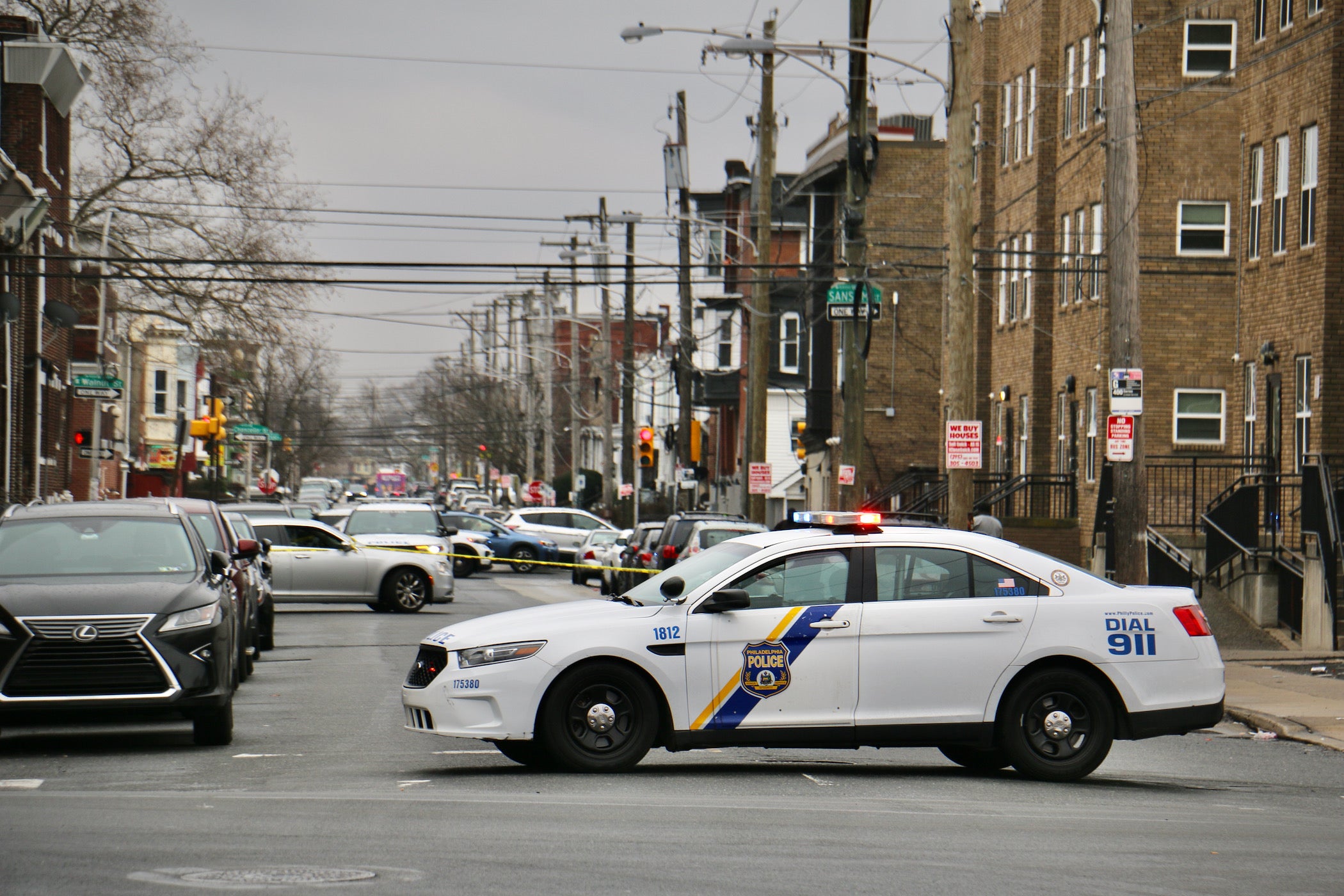 A police car parked in the middle of the road with a crime scene in the background.
